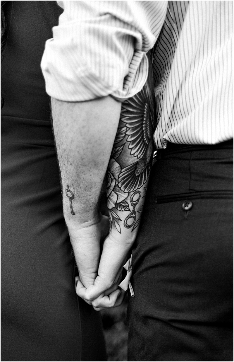 Black and white photo of two people holding hands in snohomish One has a large floral tattoo on their forearm and a key tattoo on their wrist both wear long sleeved shirts and stand close together Snohomish wedding photography