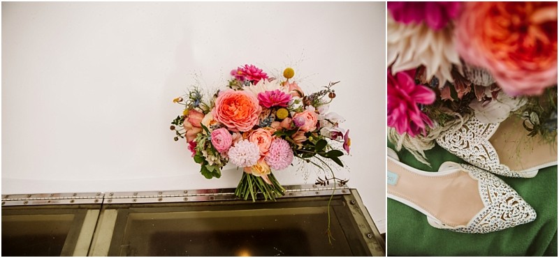 A colorful bouquet of flowers including pink peach and orange blooms with greenery sits on a glass surface in a snohomish setting Next to it a pair of white lace bridal flats rest on a green background Snohomish wedding photography