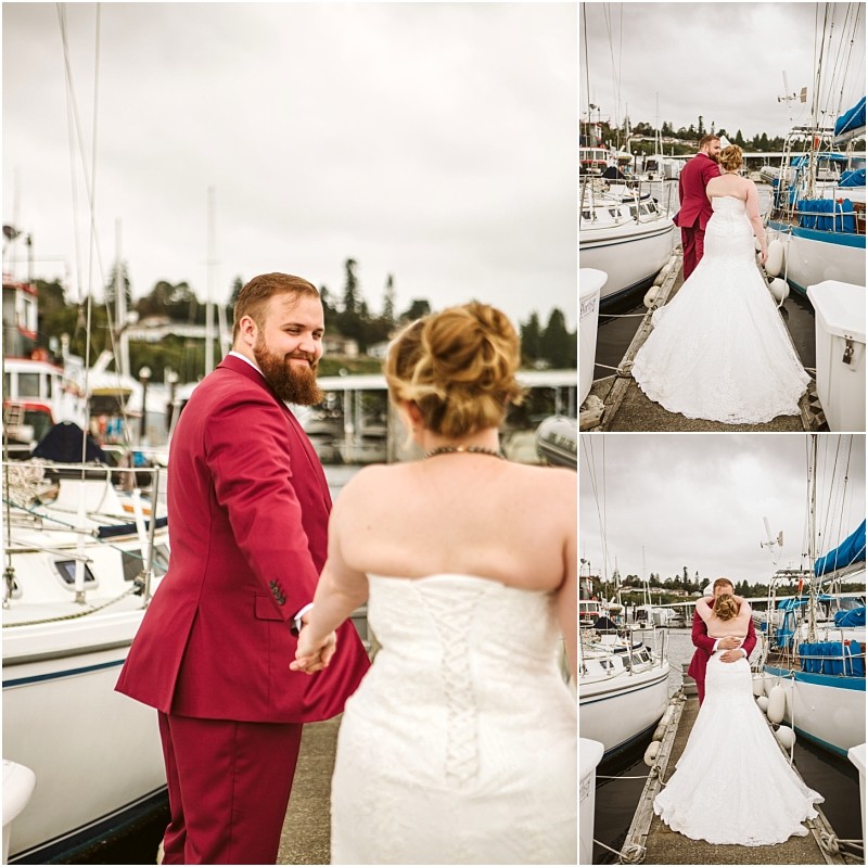 A bride in a strapless white gown and a groom in a burgundy suit hold hands and smile at each other while walking by boats in the snohomish marina on a cloudy day Snohomish wedding photography