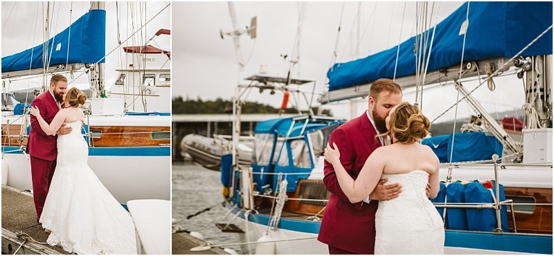 A bride in a white gown and a groom in a maroon suit embrace and share a moment by a docked sailboat with blue covers on a cloudy day in snohomish Snohomish wedding photography