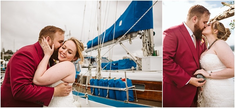 A bride and groom embrace and kiss in front of a sailboat at the snohomish marina The groom wears a red suit and the bride is in a white wedding dress looking joyful and affectionate on their special day Snohomish wedding photography
