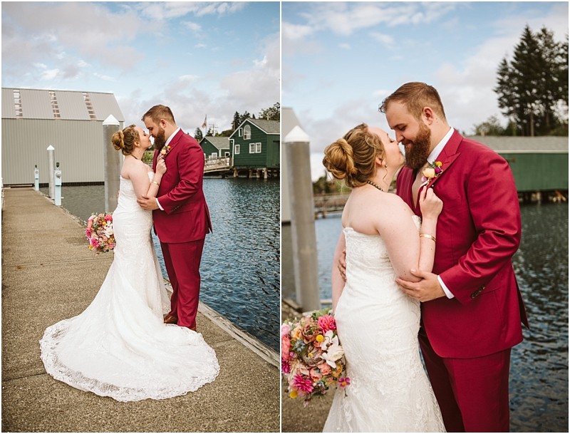 A bride in a white lace gown and a groom in a maroon suit embrace and smile at each other on a snohomish dock by the water with charming boathouses and flowers in the background Snohomish wedding photography