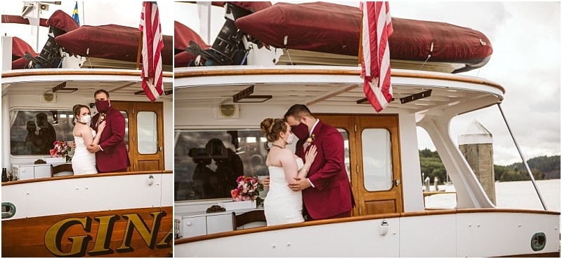 A bride and groom both wearing face masks embrace on the deck of a snohomish boat decorated with flowers and an american flag The groom wears a burgundy suit and the bride wears a white dress Snohomish wedding photography