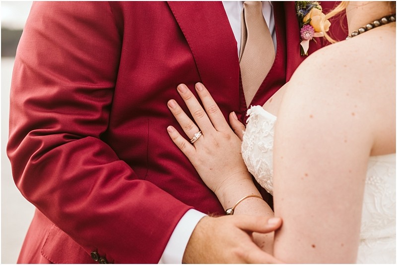 Close up of a couple embracing in snohomish with one in a red suit and tan tie the other in a white lace wedding dress gently resting a hand with a wedding ring on the suit Snohomish wedding photography