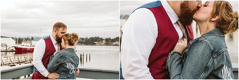 A couple stands on a waterfront deck in snohomish the man wears a red vest and white shirt while the woman in a denim jacket reading mrs  embraces and kisses him Boats and water glide by in the background Snohomish wedding photography
