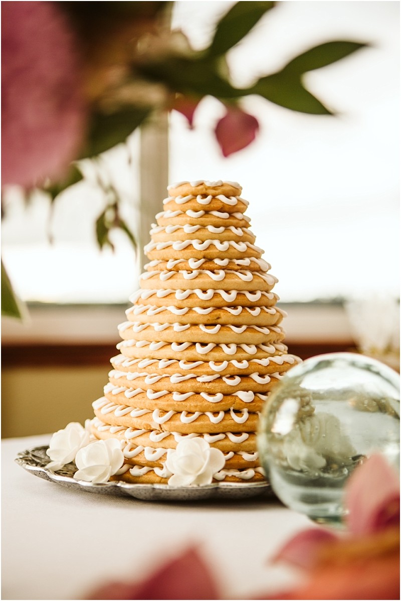 A traditional scandinavian kransekake made of stacked almond cookie rings with white icing is displayed on a tray surrounded by decorative white flowers and a glass orb in a cozy snohomish setting Snohomish wedding photography