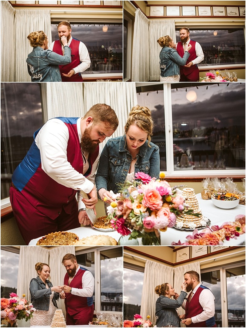 A couple in wedding attire with the bride in a denim jacket cut cake and feed each other in a cozy flower filled snohomish room with large windows showing a cloudy sky Snohomish wedding photography