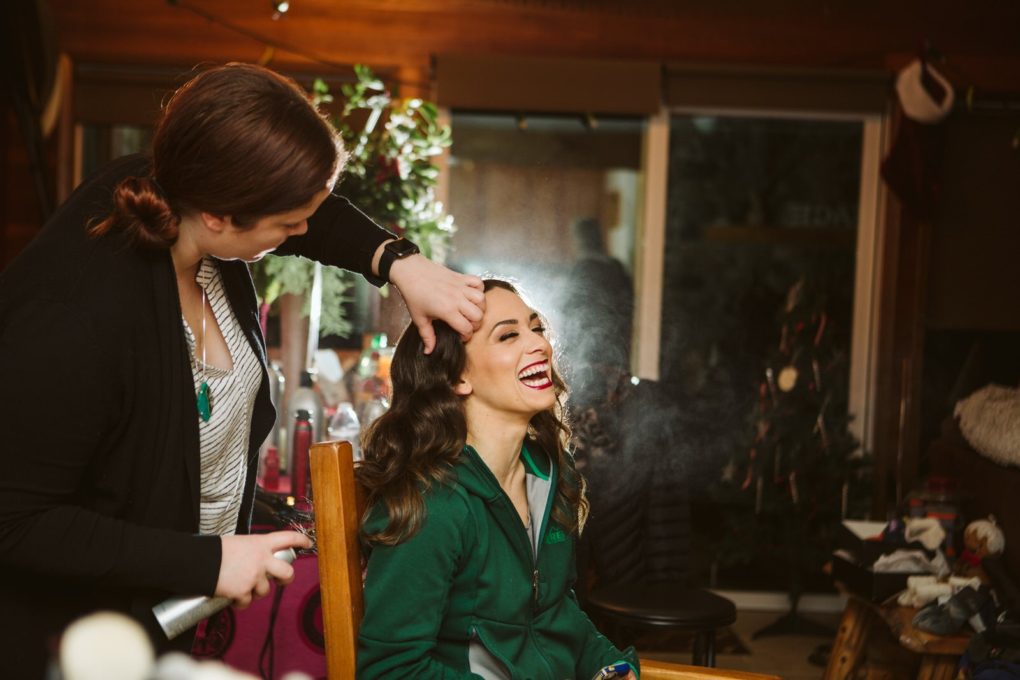 A woman with long brown hair sits smiling broadly while another person styles her hair and sprays hairspray The cheerful scene set in snohomish features various items and a christmas tree in the background Snohomish wedding photography A woman with long brown hair sits smiling broadly while another person styles her hair and sprays hairspray The cheerful scene set in snohomish features various items and a christmas tree in the background Snohomish wedding photography