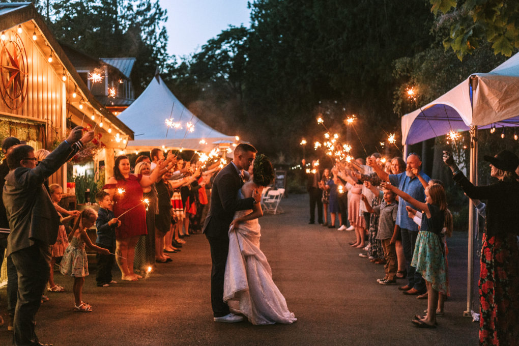 A bride and groom share a kiss outdoors at dusk in snohomish surrounded by guests holding sparklers in celebration forming two festive lines along a lit pathway at a wedding reception Snohomish wedding photography A bride and groom share a kiss outdoors at dusk in snohomish surrounded by guests holding sparklers in celebration forming two festive lines along a lit pathway at a wedding reception Snohomish wedding photography