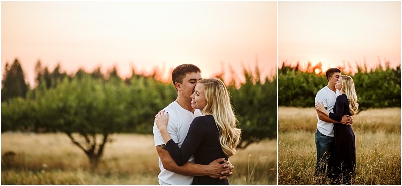 A couple stands in a grassy snohomish field at sunset The man in a white shirt embraces and kisses the forehead of the woman who has long blonde hair and wears a dark dress Trees and a warm sky are in the background Snohomish wedding photography