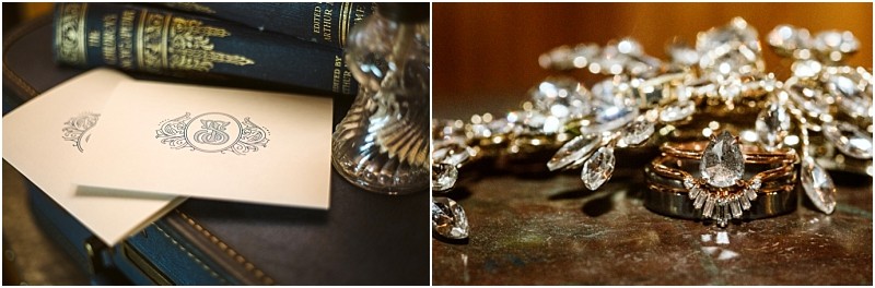 Two cream colored envelopes with an elegant monogram rest beside ornate books and a glass Nearby sparkling diamond jewelry including rings and a jeweled hairpiece shimmers on a reflective surfacecapturing timeless snohomish sophistication Snohomish wedding photography