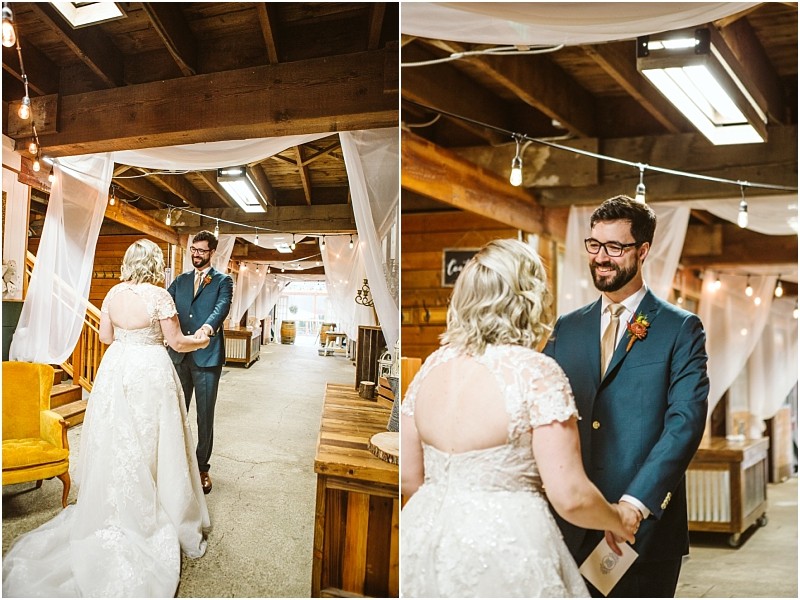 A bride in a white lace gown and a groom in a blue suit share a joyful first look inside a warmly lit rustic snohomish venue decorated with string lights and white drapery Snohomish wedding photography