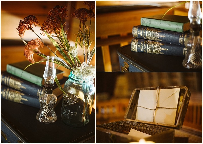 A vintage snohomish scene with stacked old books a glass oil lamp a blue mason jar holding dried flowers and an open chest of tied envelopes all set on dark luggage in a warmly lit wooden room Snohomish wedding photography