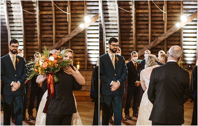 A bride in a white dress hugs an older man holding a bouquet while groomsmen in suits watch and smile in a warmly lit rustic snohomish venue with wooden walls Snohomish wedding photography