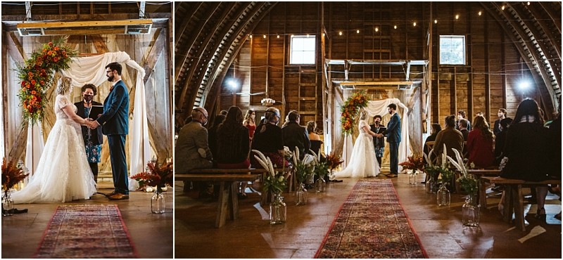 A bride and groom stand under a floral arch holding hands during their wedding ceremony inside a rustic snohomish barn with guests seated on benches and warm string lights above Snohomish wedding photography