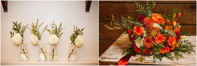 Four glass vases with white flowers and greenery sit on a shelf in snohomish next to a vibrant bouquet of orange roses white blooms and greenery on a rustic wooden table Snohomish wedding photography