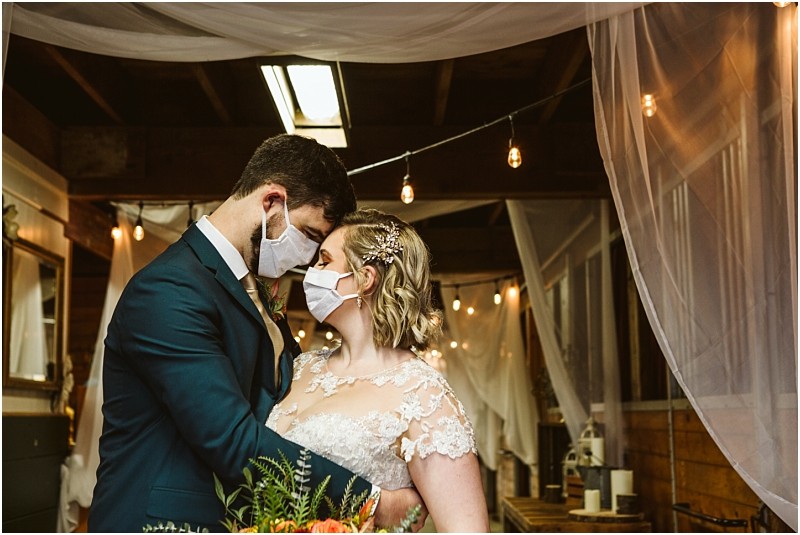 A bride and groom wearing face masks embrace closely at a snohomish indoor wedding venue decorated with string lights and sheer white fabric creating a warm and intimate atmosphere Snohomish wedding photography