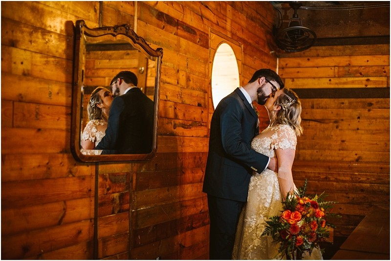 A bride and groom stand closely together in a warmly lit wooden room in snohomish gazing at each other lovingly The bride holds a colorful bouquet and their reflection is visible in an ornate wall mirror Snohomish wedding photography