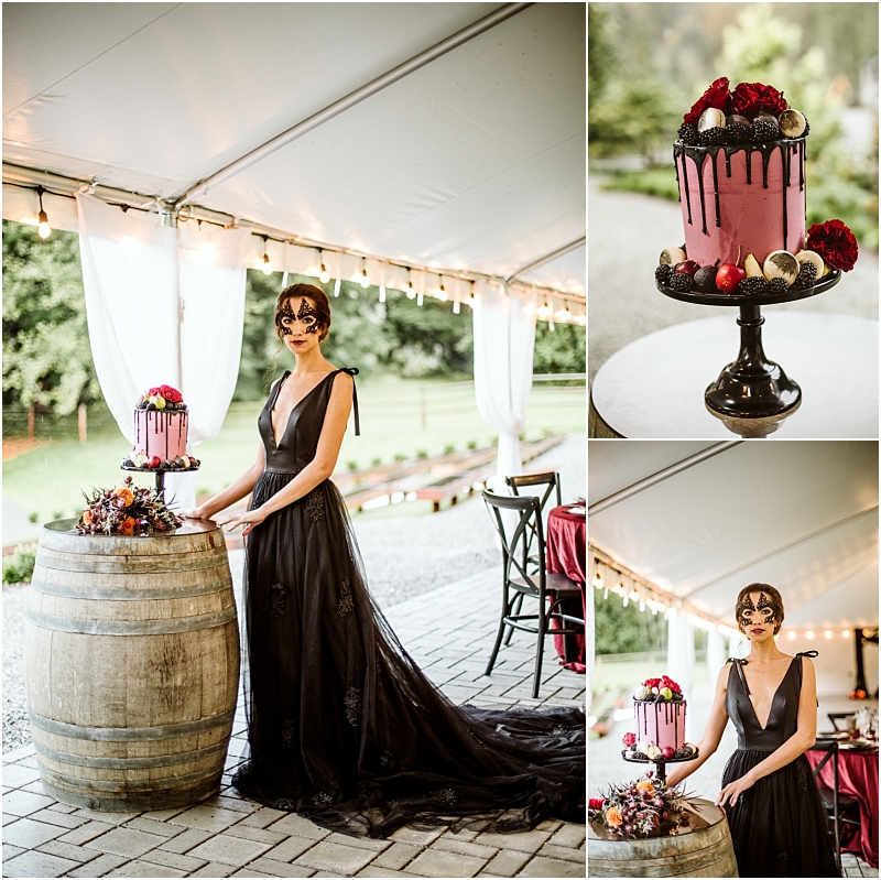 A woman in a black gown and mask stands by a wine barrel at a snohomish event showcasing a pink cake decorated with dark chocolate drip berries and figs The tent is adorned with string lights highlighting the cakes detail in close up shots Snohomish wedding photography