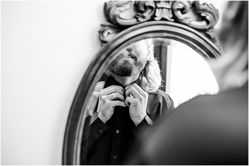 Black and white photo of a person in snohomish adjusting their shirt collar in front of an ornate mirror with their face partially visible and hands near the neck Snohomish wedding photography