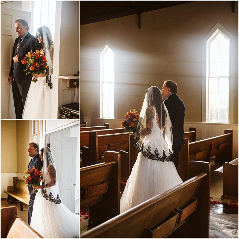 A bride in a white dress with black lace and a veil walks down a sunlit snohomish church aisle with a man holding a bouquet of orange flowers The scene is warm and intimate with wooden pews and tall windows Snohomish wedding photography