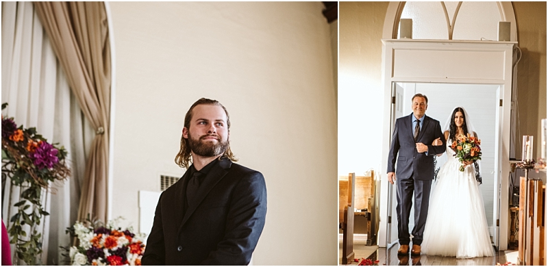 A groom in a black suit waits by floral arrangements in snohomish while a bride in a white dress and veil walks down the aisle with an older man Sunlight streams through the windows above them Snohomish wedding photography