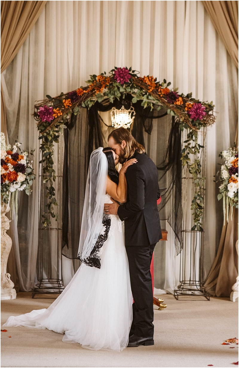 A bride and groom share a kiss at their snohomish wedding ceremony standing under a floral arch draped with black and white fabric The bride wears a white dress and veil the groom a black suit Flowers elegantly decorate the scene Snohomish wedding photography