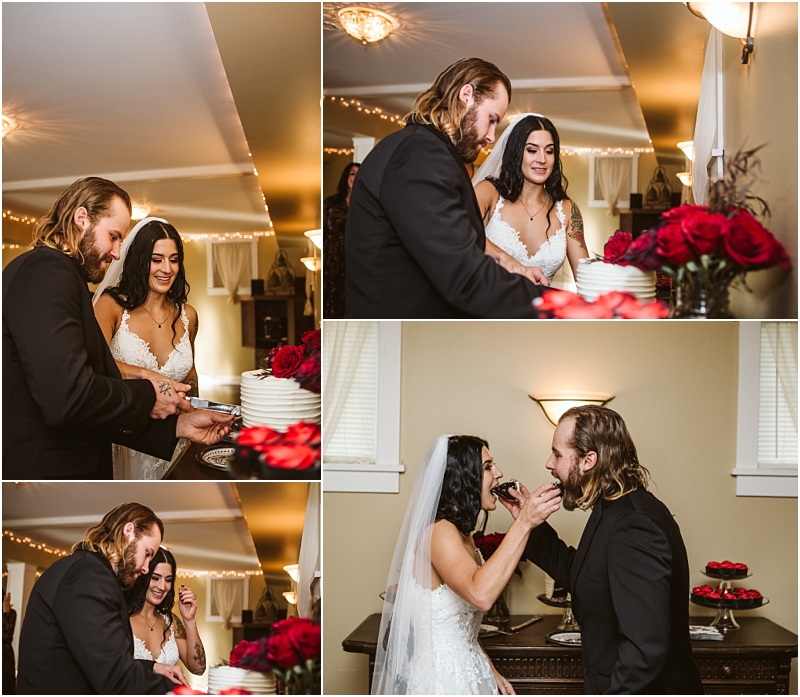 A newlywed couple in formal attire cuts their wedding cake shares a laugh and feeds each other cake in a warmly lit snohomish room beautifully decorated with red roses Snohomish wedding photography