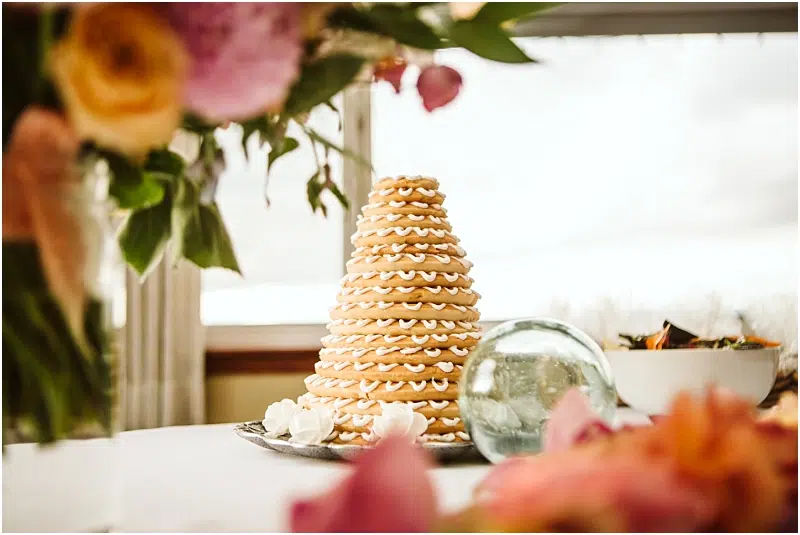 A conical stack of ring-shaped cookies decorated with white icing sits on a table in Snohomish, surrounded by flowers and a glass orb, with a bowl of food in the background. Snohomish Wedding Photography