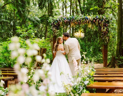 A bride and groom stand closely together under a flowercovered arch in a forest at one of the stunning Snohomish wedding venues surrounded by greenery and wooden benches the bride is in a white dress and the groom in a beige suit Snohomish Wedding Photography A bride and groom stand closely together under a flower-covered arch in a forest at one of the stunning Snohomish wedding venues, surrounded by greenery and wooden benches; the bride is in a white dress and the groom in a beige suit. Snohomish Wedding Photography