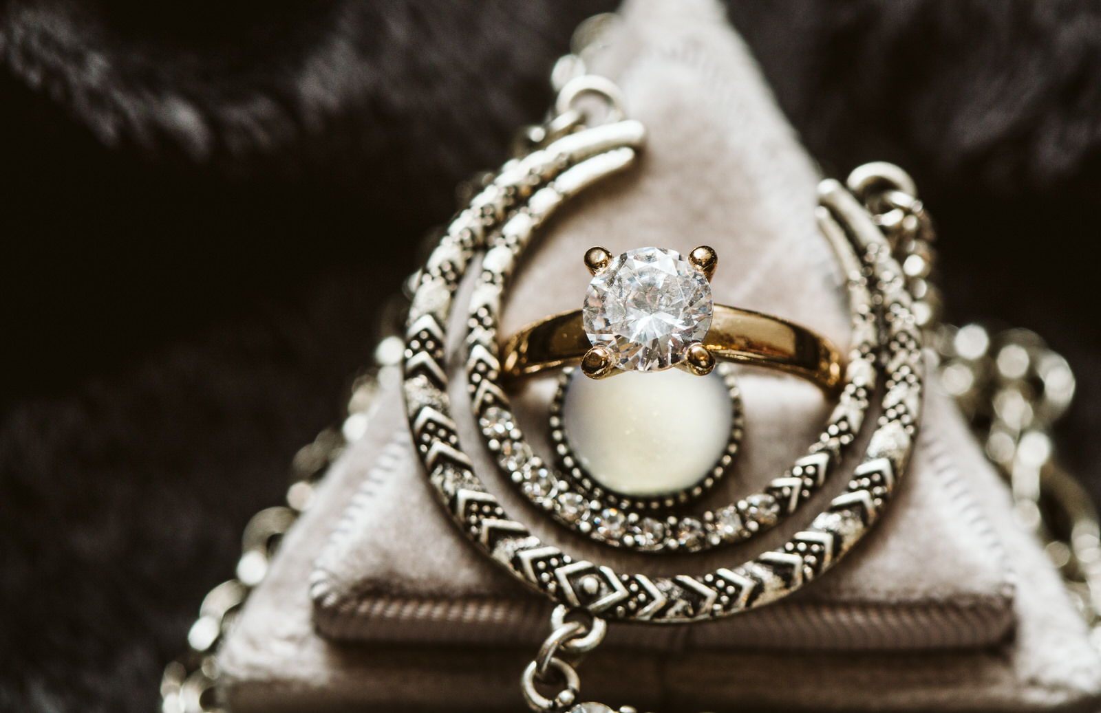 A gold ring with a large, round diamond is displayed on a soft, triangular jewelry stand in Snohomish, surrounded by intricately patterned silver bangles and chains. Snohomish Wedding Photography