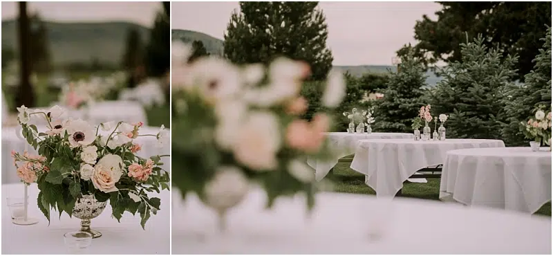 Outdoor event setup in Snohomish with round tables covered in white cloths, each decorated with elegant floral centerpieces and greenery. The scene is set on a lawn with trees and mountains in the background. Snohomish Wedding Photography