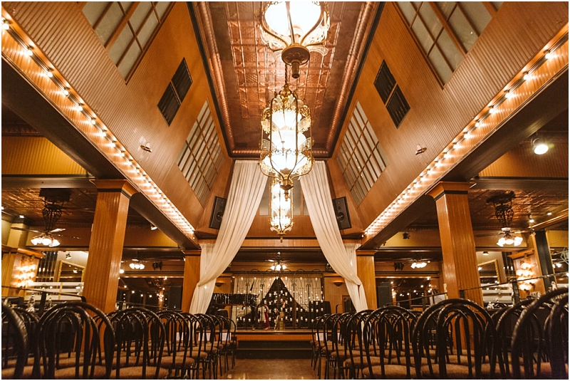 Elegant snohomish indoor event space with rows of dark chairs facing a stage warm lighting from chandeliers tall columns draped white curtains and a large mirror at the back reflecting the room Snohomish wedding photography