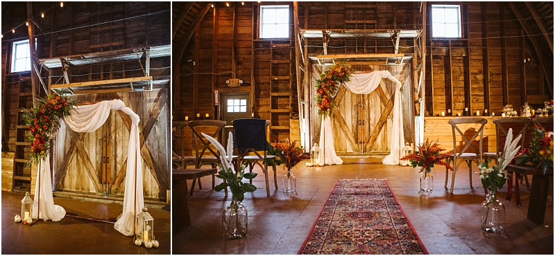 A rustic indoor wedding setup in snohomish features a wooden barn backdrop with draped white fabric and a floral arrangement Chairs line a patterned rug aisle vases with flowers decorate the path and warm lighting fills the space Snohomish wedding photography
