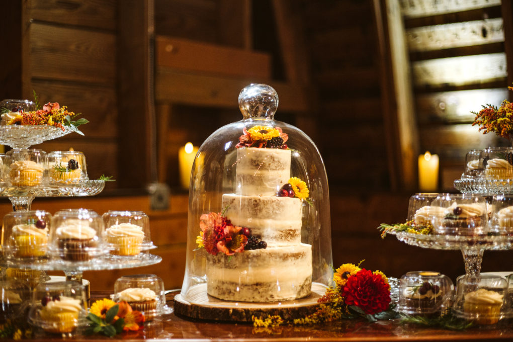 Socially distanced reception with individually packaged cupcakes and wedding cake inside a cloche for covid pandemic restrictions
