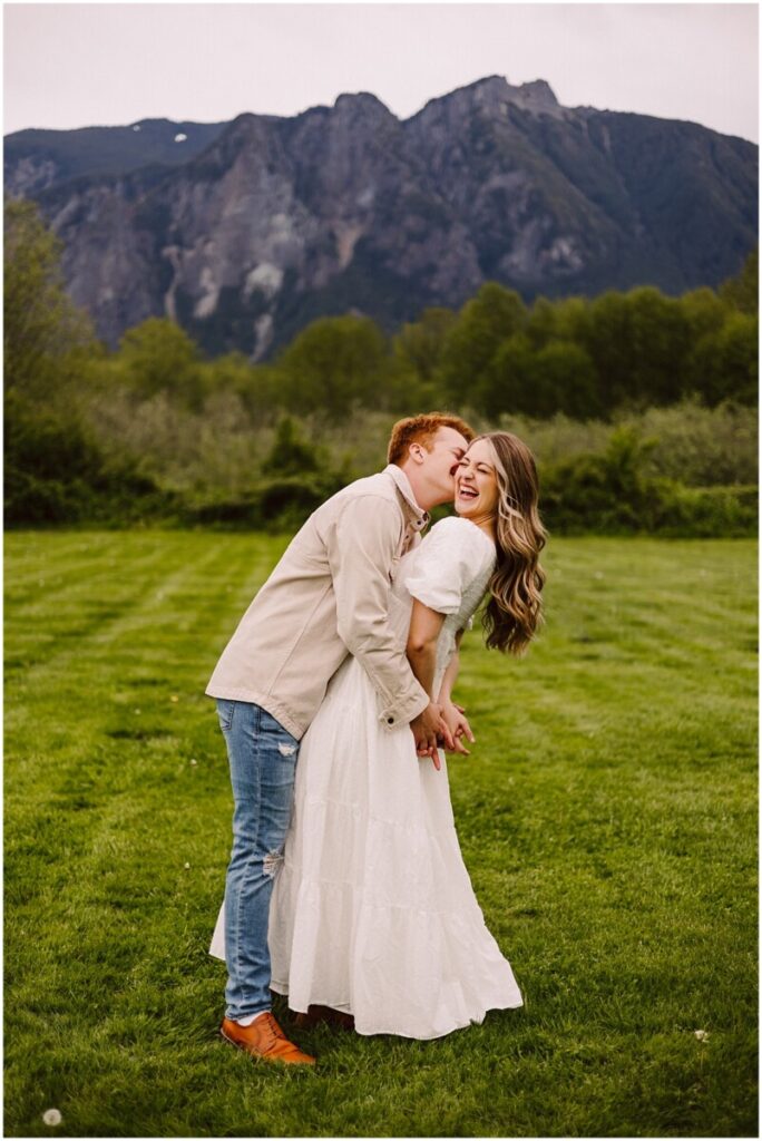 Meadowbrook farm engagement with mt si in the background with girl in white dress being kissed by red haired man
