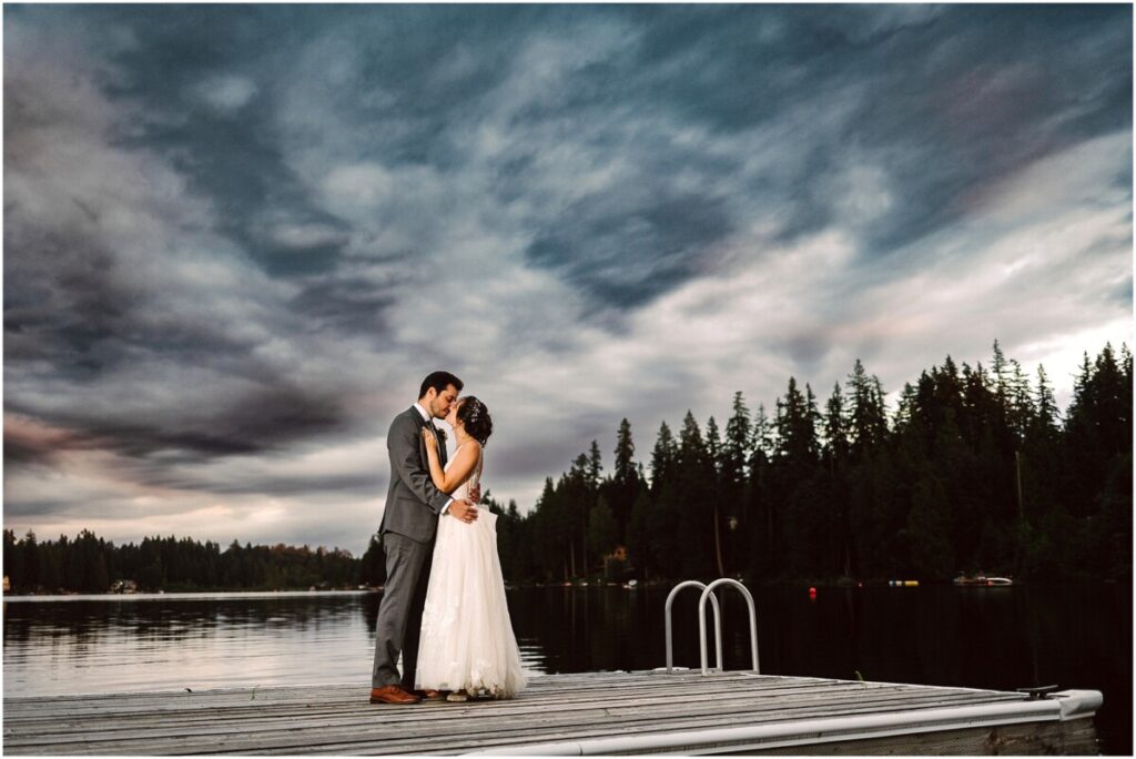 Green gates at flowing lake wedding bride and groom on the dock during a stormy sunset kissing Green gates at flowing lake wedding bride and groom on the dock during a stormy sunset kissing