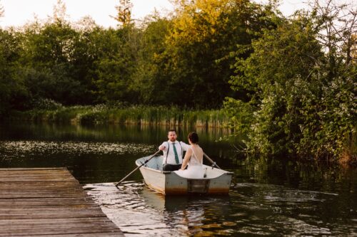 A couple in formal attire sits in a small rowboat on a calm lake near a wooden dock surrounded by lush green trees and bushes at sunsetcapturing the romantic charm found at many beautiful Snohomish wedding venues Snohomish Wedding Photography A couple in formal attire sits in a small rowboat on a calm lake near a wooden dock, surrounded by lush green trees and bushes at sunset—capturing the romantic charm found at many beautiful Snohomish wedding venues. Snohomish Wedding Photography