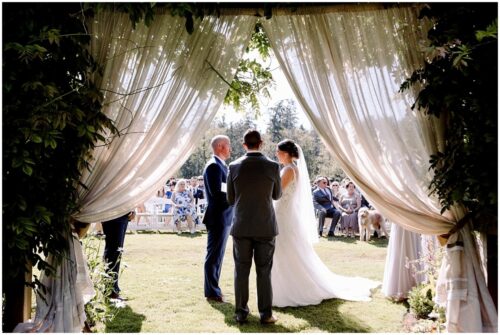 A bride and groom stand facing each other at an outdoor ceremony framed by sheer curtains and greenery with guests on white chairs Many Snohomish wedding venues offer similar picturesque settings for your special day Snohomish Wedding Photography A bride and groom stand facing each other at an outdoor ceremony, framed by sheer curtains and greenery, with guests on white chairs. Many Snohomish wedding venues offer similar picturesque settings for your special day. Snohomish Wedding Photography
