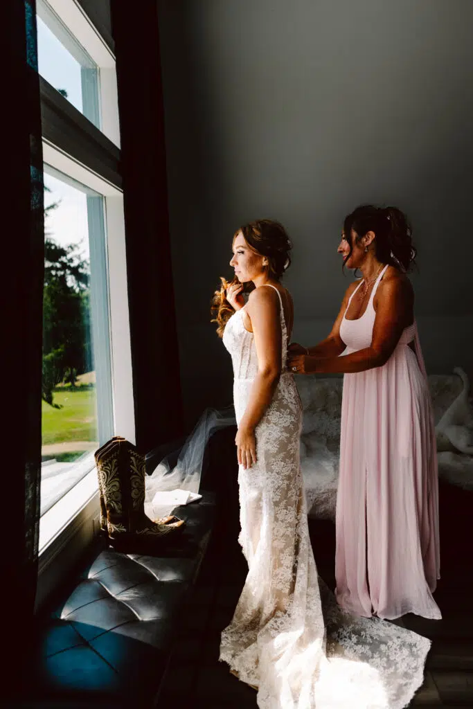 Snohomish Wedding Photographer GSquared Weddings A bride in a lace gown stands near a window her mother in a light pink dress lovingly adjusting her attire Sunlight streams in illuminating their figures A pair of cowboy boots rests on the windowsill honoring moms love for country flair at the wedding Serving Seattle Snohomish and Washington State Snohomish Wedding Photographer GSquared Weddings A bride in a lace gown stands near a window, her mother in a light pink dress lovingly adjusting her attire. Sunlight streams in, illuminating their figures. A pair of cowboy boots rests on the windowsill, honoring moms love for country flair at the wedding. Serving Seattle, Snohomish and Washington State
