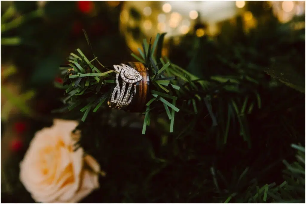 snohomishweddingphotographer8975 winter wedding with pear shaped diamond bridal wedding ring and wood inset men's wedding band on a Christmas tree branch with Christmas lights twinkling in the background