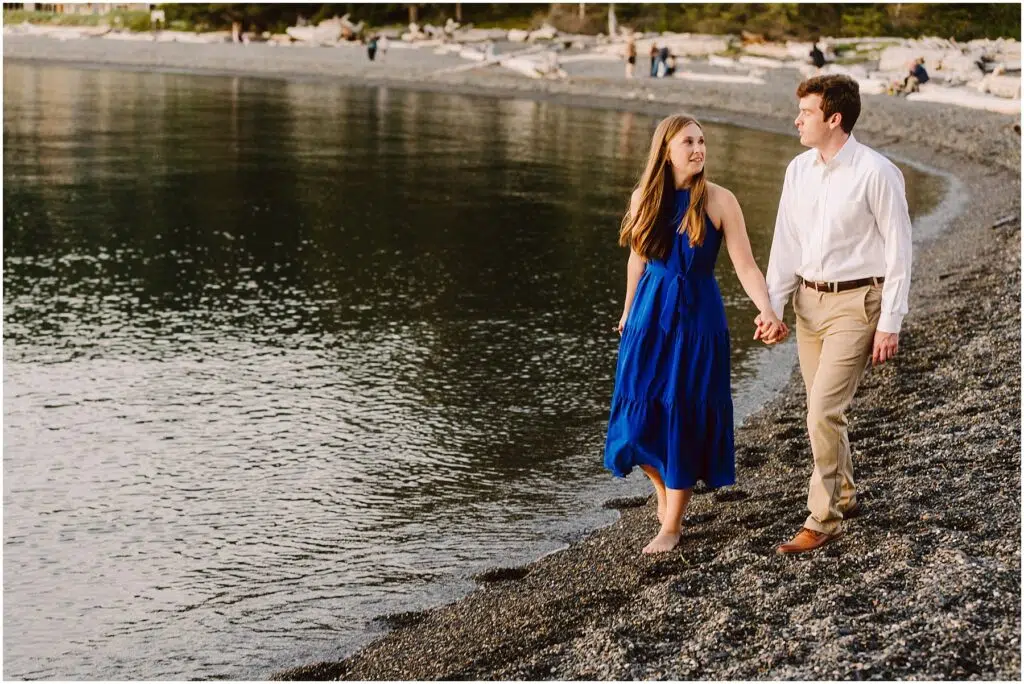 Snohomish Wedding Photographer GSquared Weddings A couple walks hand in hand along a pebbled beach The woman wears a blue dress and the man wears a white shirt and beige pants The calm water reflects the evening light and driftwood is scattered along the shore Serving Seattle Snohomish and Washington State Snohomish Wedding Photographer GSquared Weddings A couple walks hand in hand along a pebbled beach. The woman wears a blue dress, and the man wears a white shirt and beige pants. The calm water reflects the evening light, and driftwood is scattered along the shore. Serving Seattle, Snohomish and Washington State