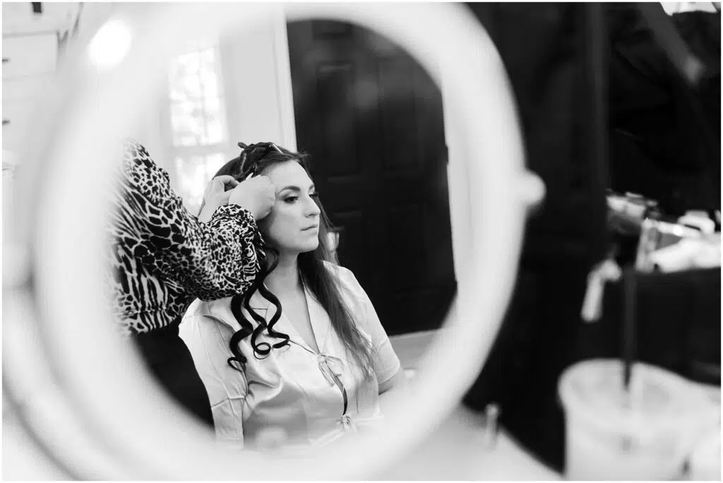 Snohomish Wedding Photographer GSquared Weddings A woman with long hair sits in front of a mirror having her hair styled by another person The scene is captured in black and white with soft lighting A drink with a straw is visible in the foreground Serving Seattle Snohomish and Washington State Snohomish Wedding Photographer GSquared Weddings A woman with long hair sits in front of a mirror, having her hair styled by another person. The scene is captured in black and white, with soft lighting. A drink with a straw is visible in the foreground. Serving Seattle, Snohomish and Washington State