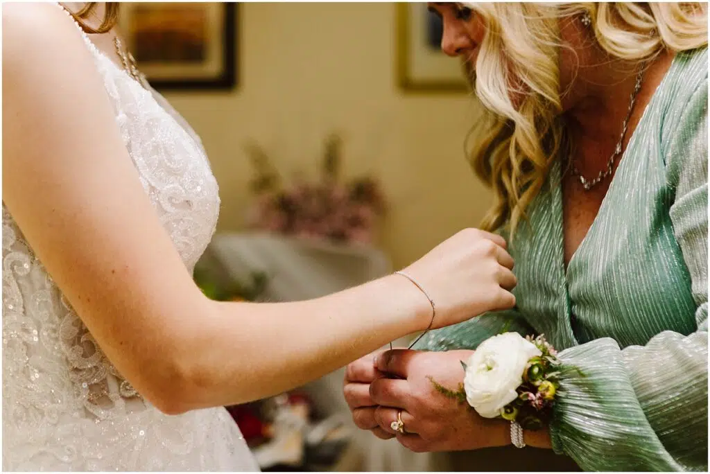 Snohomish Wedding Photographer GSquared Weddings A bride in a white lace dress assists a woman in a green dress with a white rose corsage The moment captures the intimacy and elegance of a special occasion likely a wedding Floral decor is visible in the background Serving Seattle Snohomish and Washington State Snohomish Wedding Photographer GSquared Weddings A bride in a white lace dress assists a woman in a green dress with a white rose corsage. The moment captures the intimacy and elegance of a special occasion, likely a wedding. Floral decor is visible in the background. Serving Seattle, Snohomish and Washington State