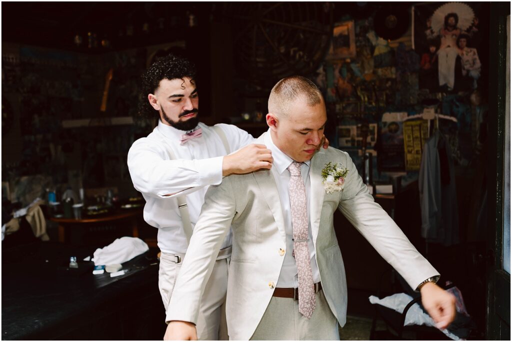 Snohomish wedding photographer gsquared weddings a groom in a beige suit is being helped with his jacket by a groomsman wearing a white outfit and pink bow tie They are standing in a room with eclectic decorations and artwork on the walls Serving seattle snohomish and washington state Snohomish wedding photographer gsquared weddings a groom in a beige suit is being helped with his jacket by a groomsman wearing a white outfit and pink bow tie They are standing in a room with eclectic decorations and artwork on the walls Serving seattle snohomish and washington state