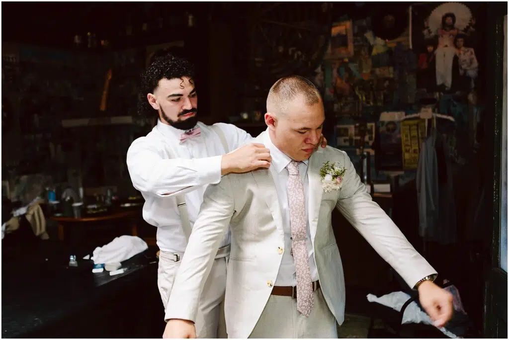 Snohomish Wedding Photographer GSquared Weddings A groom in a beige suit is being helped with his jacket by a groomsman wearing a white outfit and pink bow tie They are standing in a room with eclectic decorations and artwork on the walls Serving Seattle Snohomish and Washington State Snohomish Wedding Photographer GSquared Weddings A groom in a beige suit is being helped with his jacket by a groomsman wearing a white outfit and pink bow tie. They are standing in a room with eclectic decorations and artwork on the walls. Serving Seattle, Snohomish and Washington State