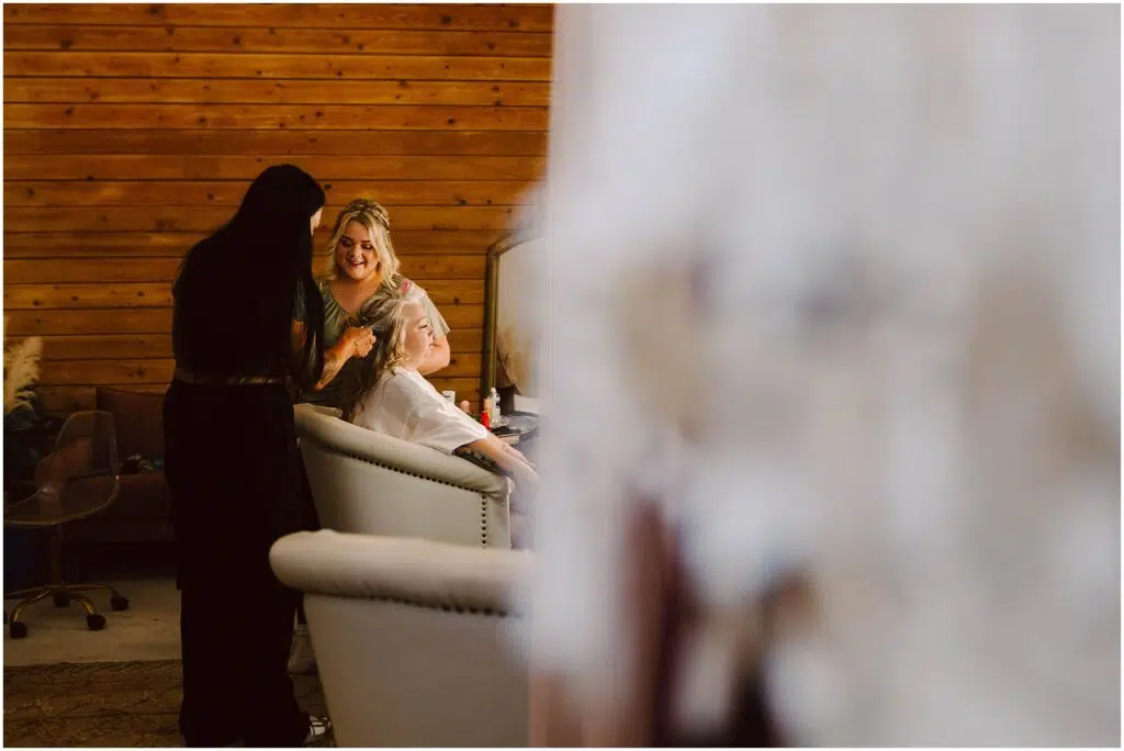 Snohomish Wedding Photographer GSquared Weddings Two women style another womans hair and makeup in a salon with wooden walls The seated woman is smiling while two stylists work on her Blurred foreground elements frame the scene adding depth to the cozy setting Serving Seattle Snohomish and Washington State Snohomish Wedding Photographer GSquared Weddings Two women style another womans hair and makeup in a salon with wooden walls. The seated woman is smiling while two stylists work on her. Blurred foreground elements frame the scene, adding depth to the cozy setting. Serving Seattle, Snohomish and Washington State