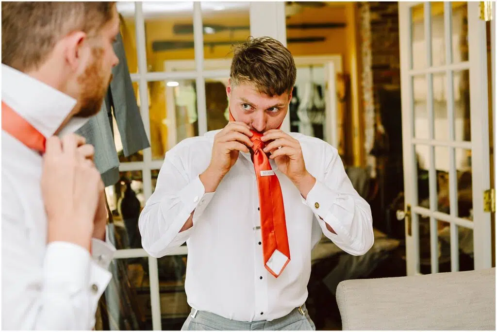 Snohomish Wedding Photographer GSquared Weddings A person in a white shirt reflected in a mirror bites open the packaging of an orange tie in a room with glasspaneled doors and a suit hanging in the background Serving Seattle Snohomish and Washington State Snohomish Wedding Photographer GSquared Weddings A person in a white shirt, reflected in a mirror, bites open the packaging of an orange tie in a room with glass-paneled doors and a suit hanging in the background. Serving Seattle, Snohomish and Washington State