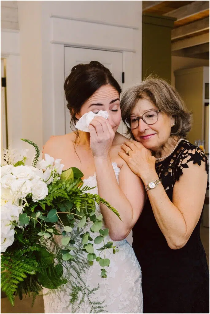 Snohomish Wedding Photographer GSquared Weddings A bride in a white dress holds a large bouquet of white flowers and greenery wiping tears from her eyes An older woman in a black dress likely a family member stands close affectionately resting her head on the brides shoulder Serving Seattle Snohomish and Washington State Snohomish Wedding Photographer GSquared Weddings A bride in a white dress holds a large bouquet of white flowers and greenery, wiping tears from her eyes. An older woman in a black dress, likely a family member, stands close, affectionately resting her head on the brides shoulder. Serving Seattle, Snohomish and Washington State