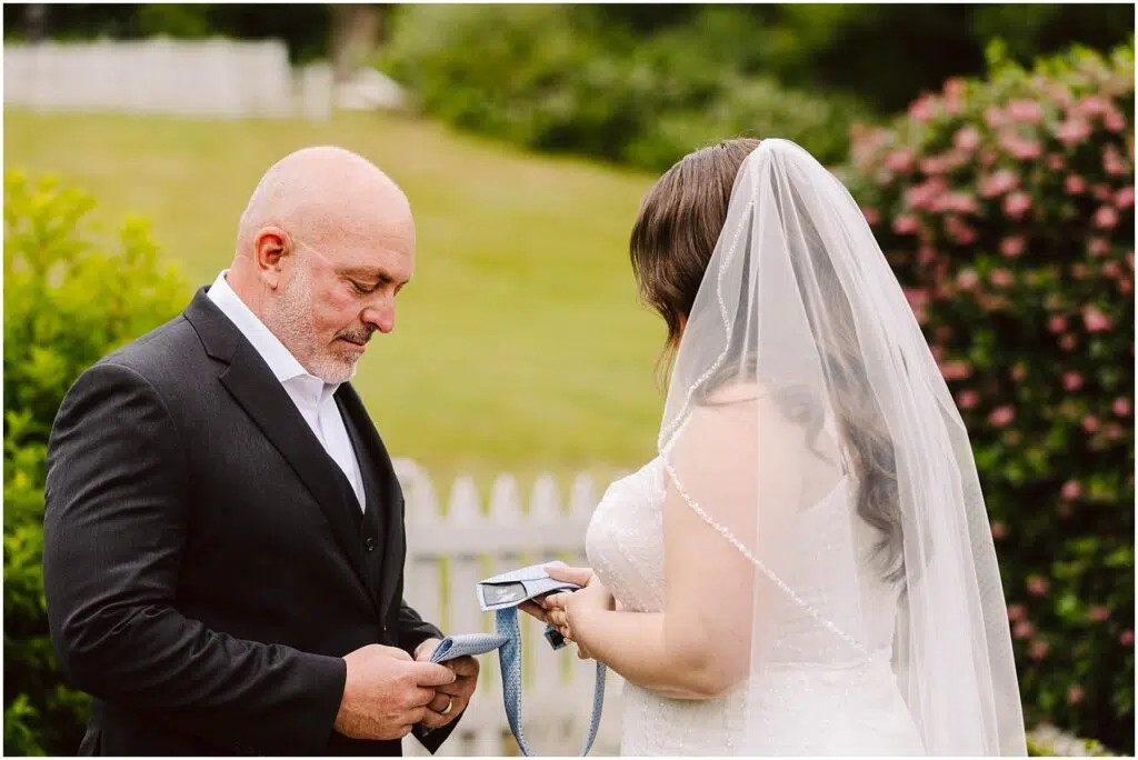 Snohomish Wedding Photographer GSquared Weddings A bride and a man in a suit possibly her father stand outdoors in a garden setting The bride facing away holds a piece of paper The man looks down at a tie in his hands A white fence and greenery are in the background Serving Seattle Snohomish and Washington State Snohomish Wedding Photographer GSquared Weddings A bride and a man in a suit, possibly her father, stand outdoors in a garden setting. The bride, facing away, holds a piece of paper. The man looks down at a tie in his hands. A white fence and greenery are in the background. Serving Seattle, Snohomish and Washington State